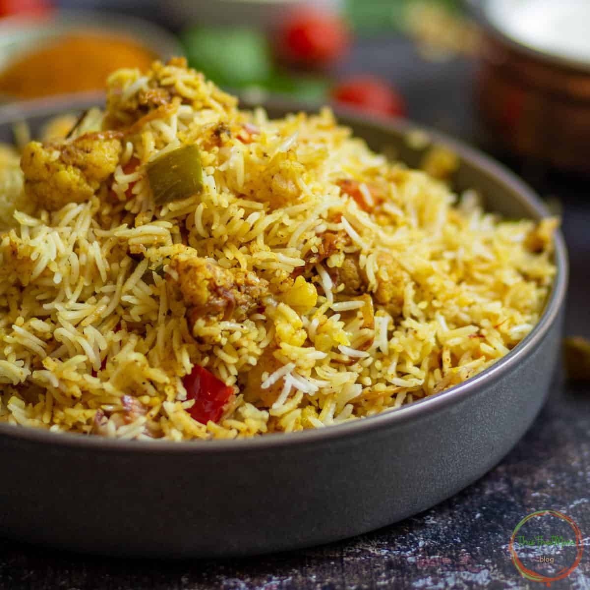 Paneer Biryani served in a grey bowl with onions and green chutney.