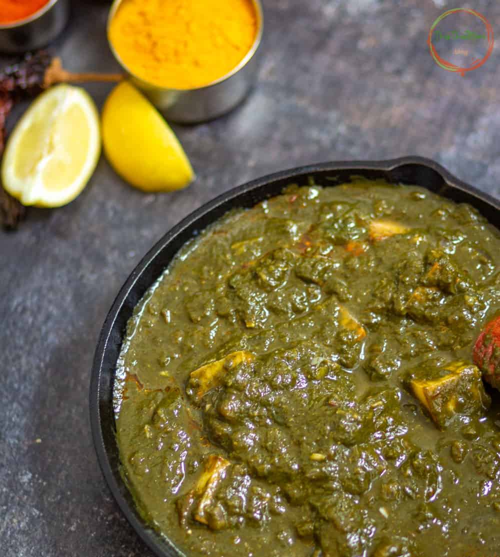 Palak Paneer in a black pan with spices on the side.