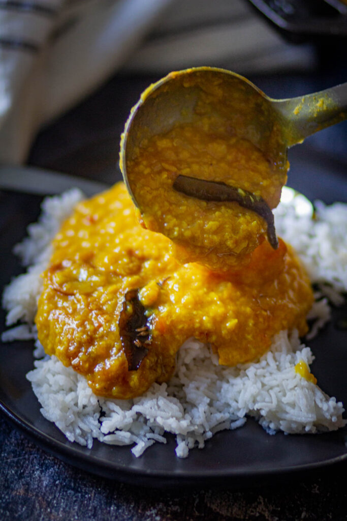 Pouring Instant Pot Moong Dal over the rice in a black plate.