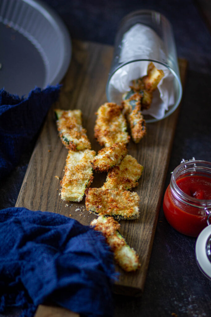 zucchini fries laying flat on the wooden cutting board with ketchup