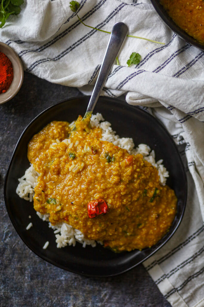 moong dal tadka on a black plate with spoon.