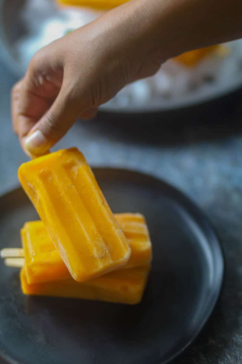 Placing mango popsicle over a stack of popsicles.