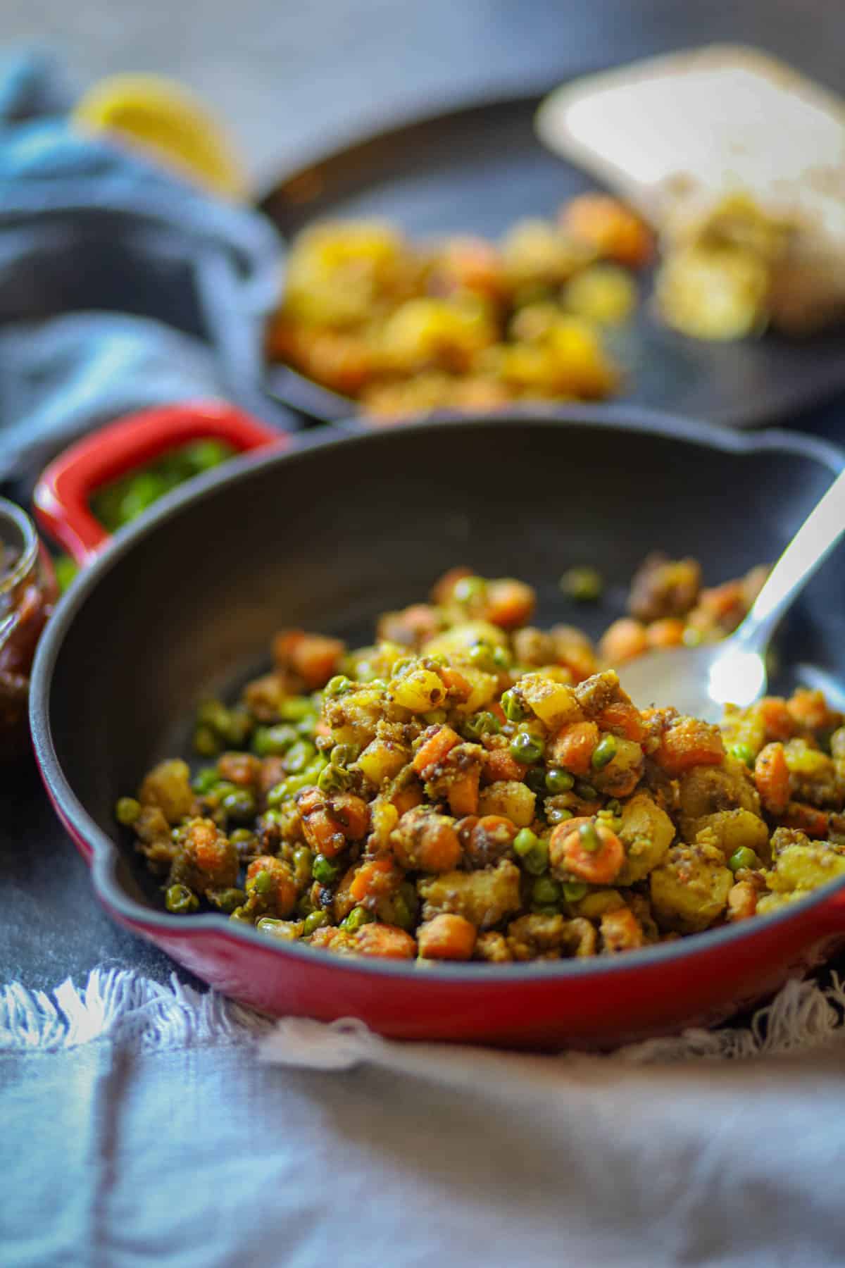 Aloo Gajar Matar serve in a red skillet with a spoon. 