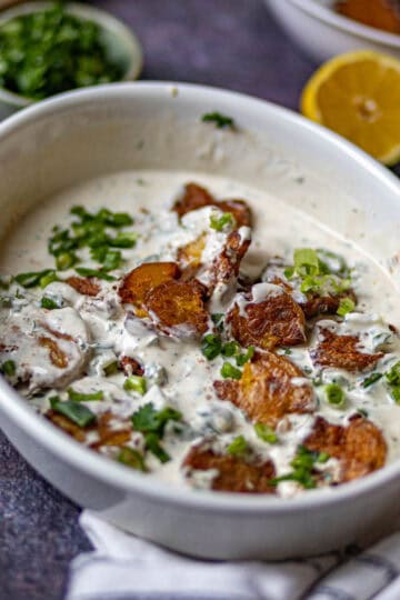 A white bowl with potatoes and green onions
